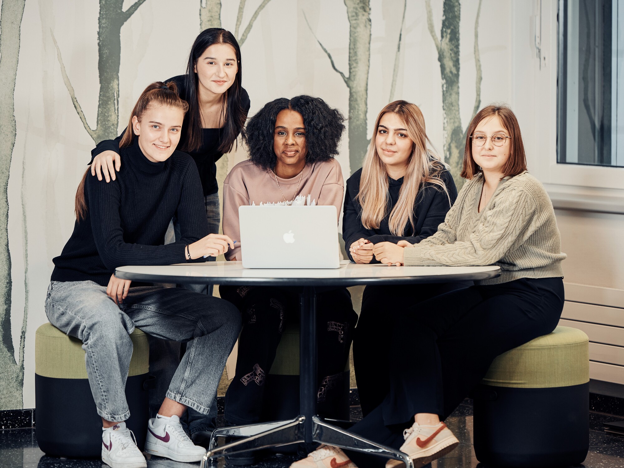 Ein Gruppenbild von fünf Personen, die an einem runden Tisch vor einem Laptop sitzen.