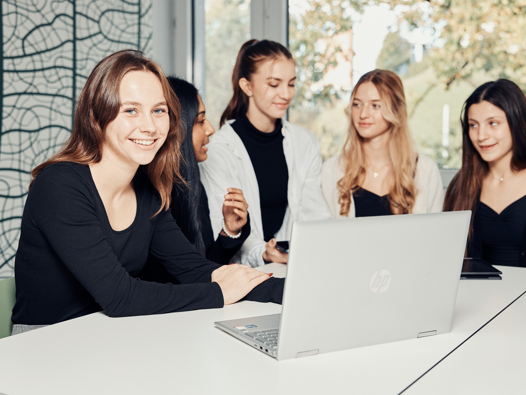 Lernen an der KV Luzern Berufsfachschule Eine Frauengruppe sitzt an einem Tisch mit Laptop und bespricht etwas, eine der jungen Frauen schaut ins Bild.