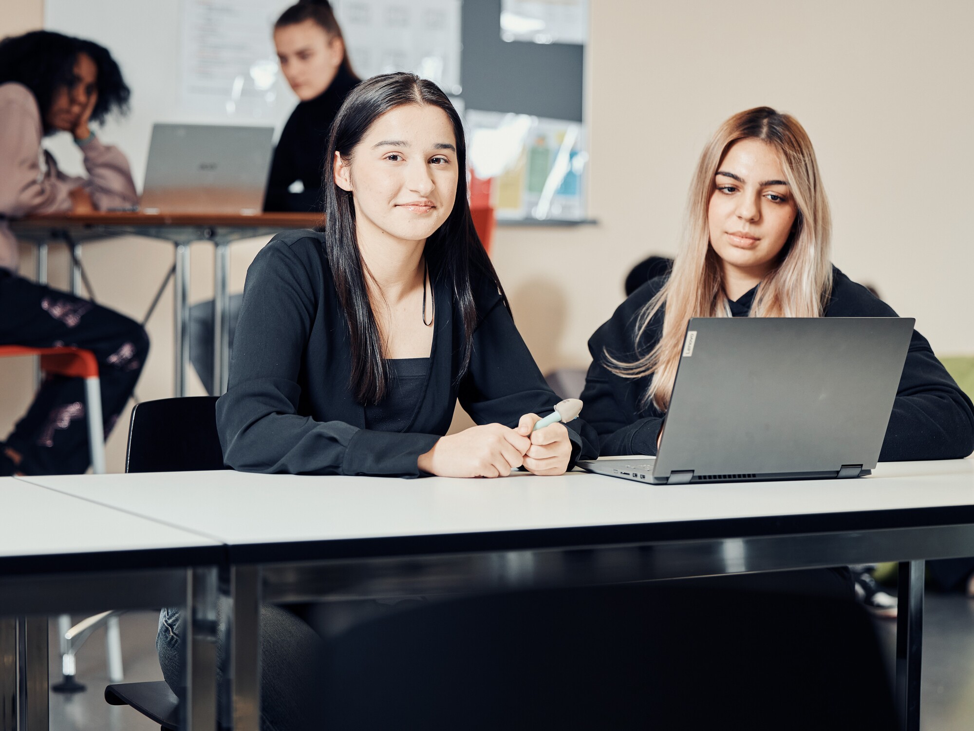 Zwei Frauen sitzen an einem Tisch und arbeiten gemeinsam an einem Laptop.
