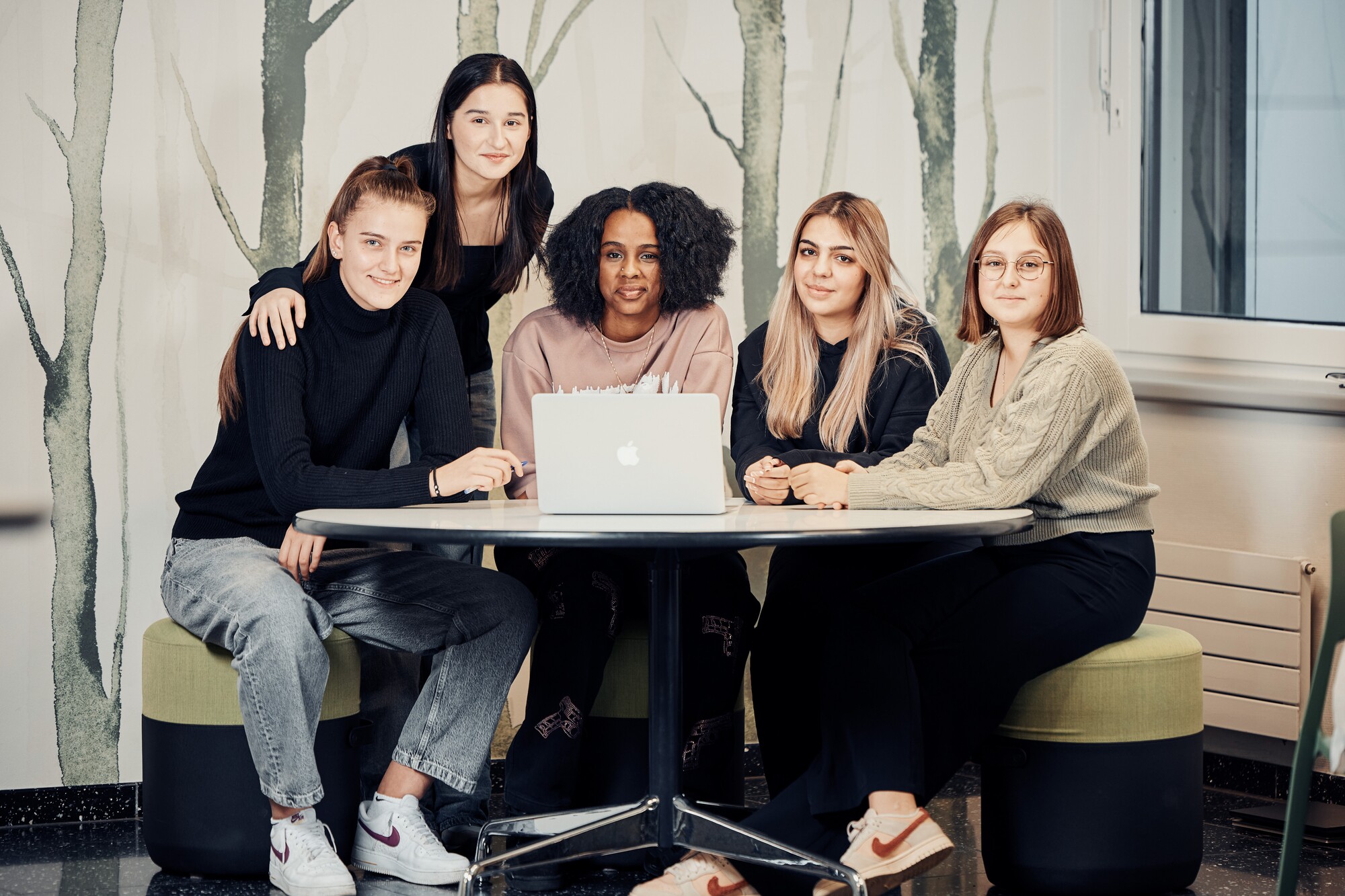 Ein Gruppenbild von fünf Personen, die an einem runden Tisch vor einem Laptop sitzen.